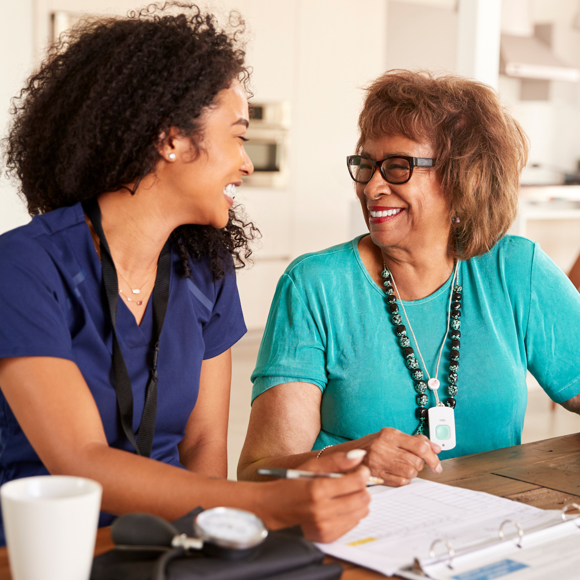 Female nurse sitting at table smiling with a senior woman during a home health visit