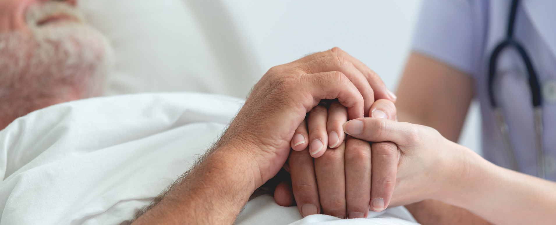 Nurse holding senior mans hand at end of life.