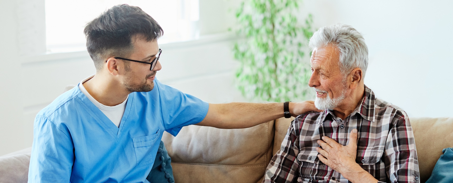 nurse talking with senior man on sofa at home or nursing home