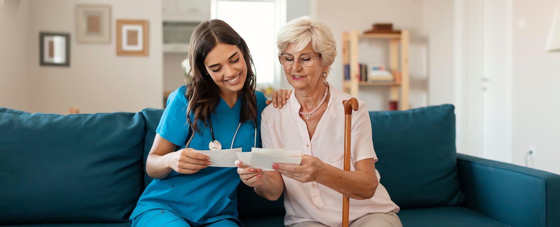 Senior woman and a private nurse sitting together on a couch looking through papers
